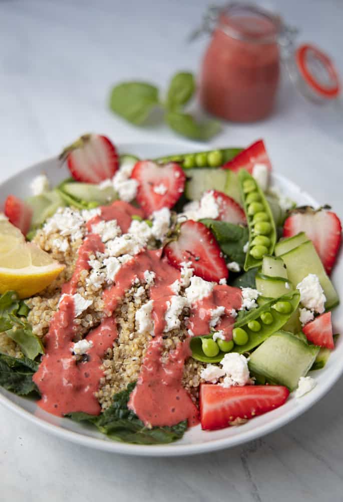 summer quinoa salad in a bowl with a drizzle of strawberry basil dressing over the top