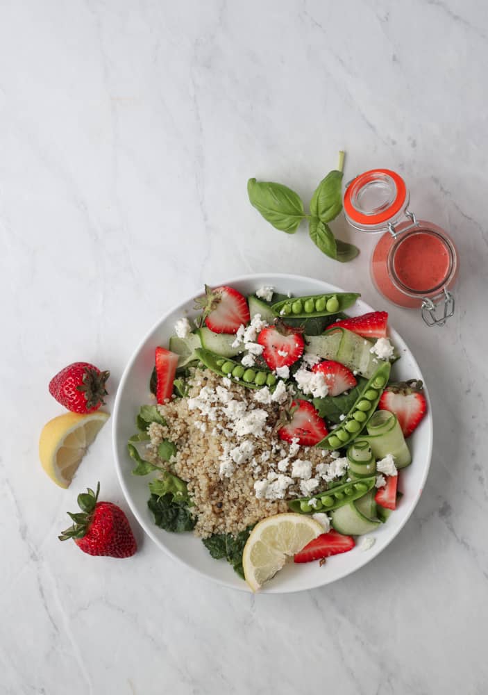 A bowl of quinoa, strawberries, snap peas and cucumber with goat cheese on top. 