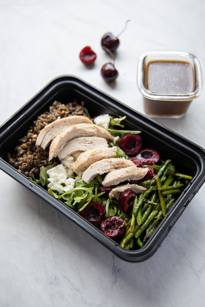 meal prep container with cherry lentil salad topped with chicken