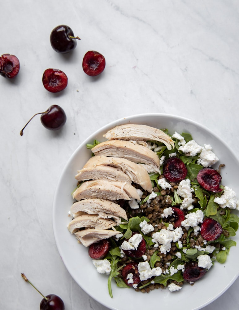 white bowl with cherry lentil salad topped with chicken