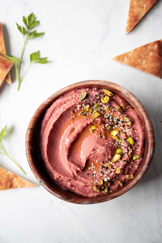 lemon beet hummus in a bowl with garnishes on top