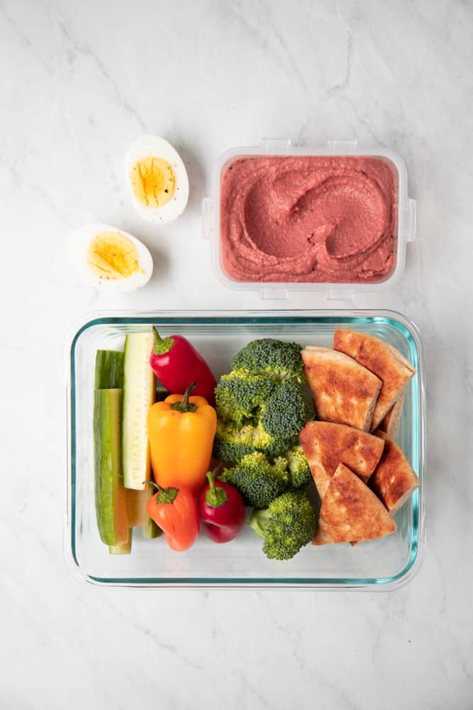 Tupperware with sliced veggies and pita bread with lemon beet hummus on the side