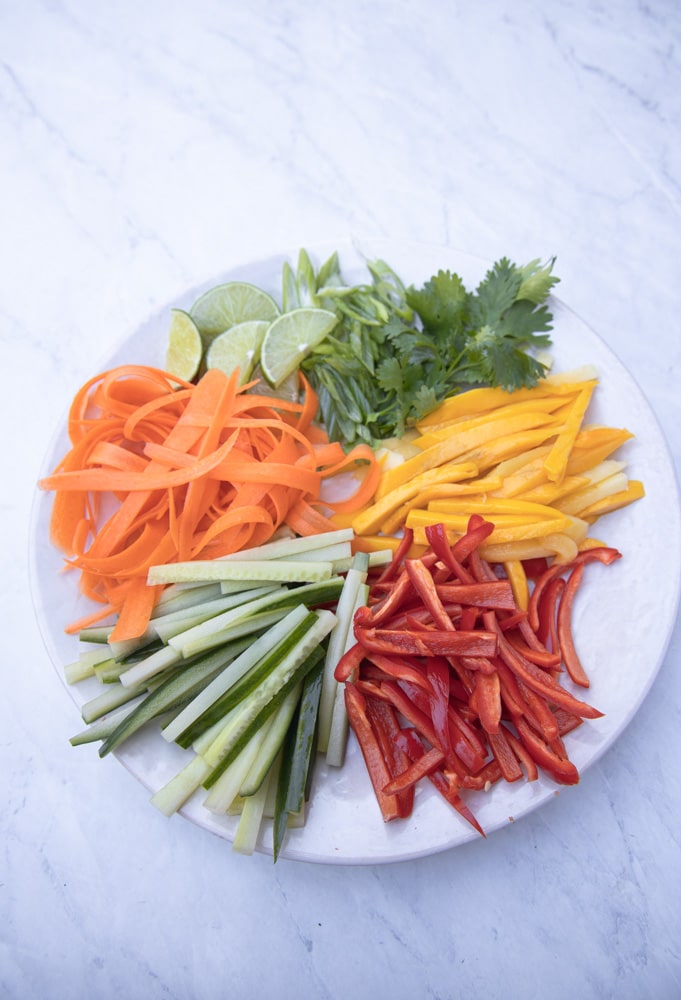 platter with chopped carrots, mango, bell pepper, cucumber, herbs and limes