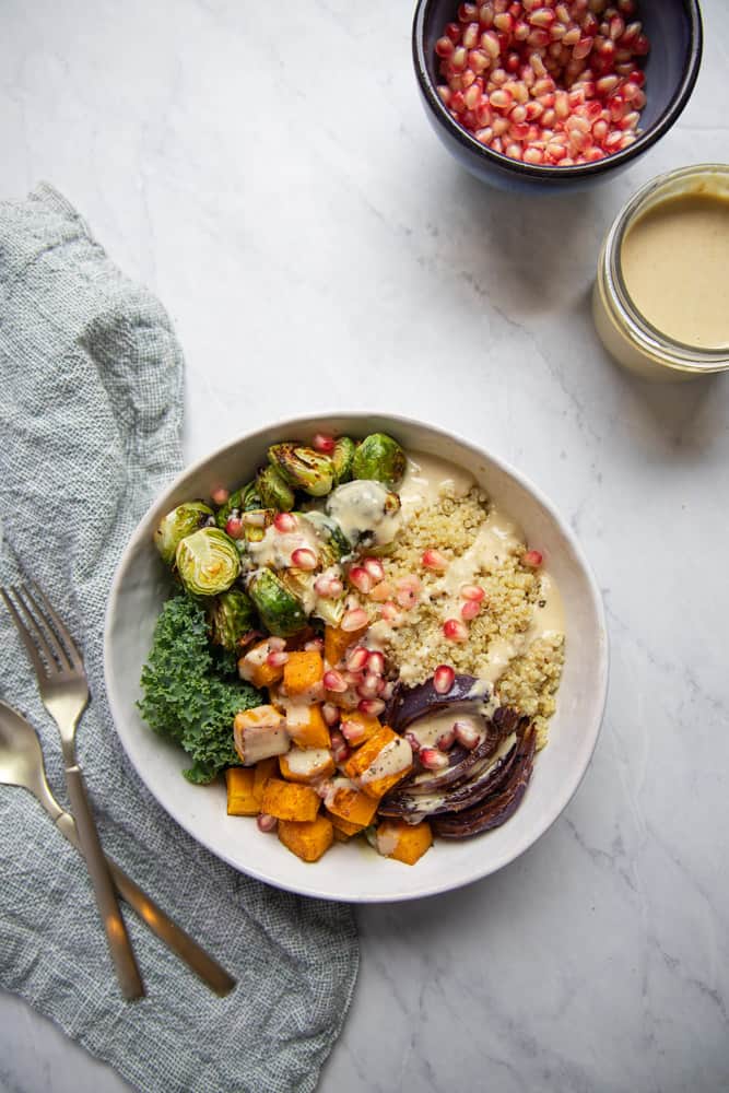 finished bowl of quinoa and roasted veggies topped with pomegranate seeds and maple tahini dressing