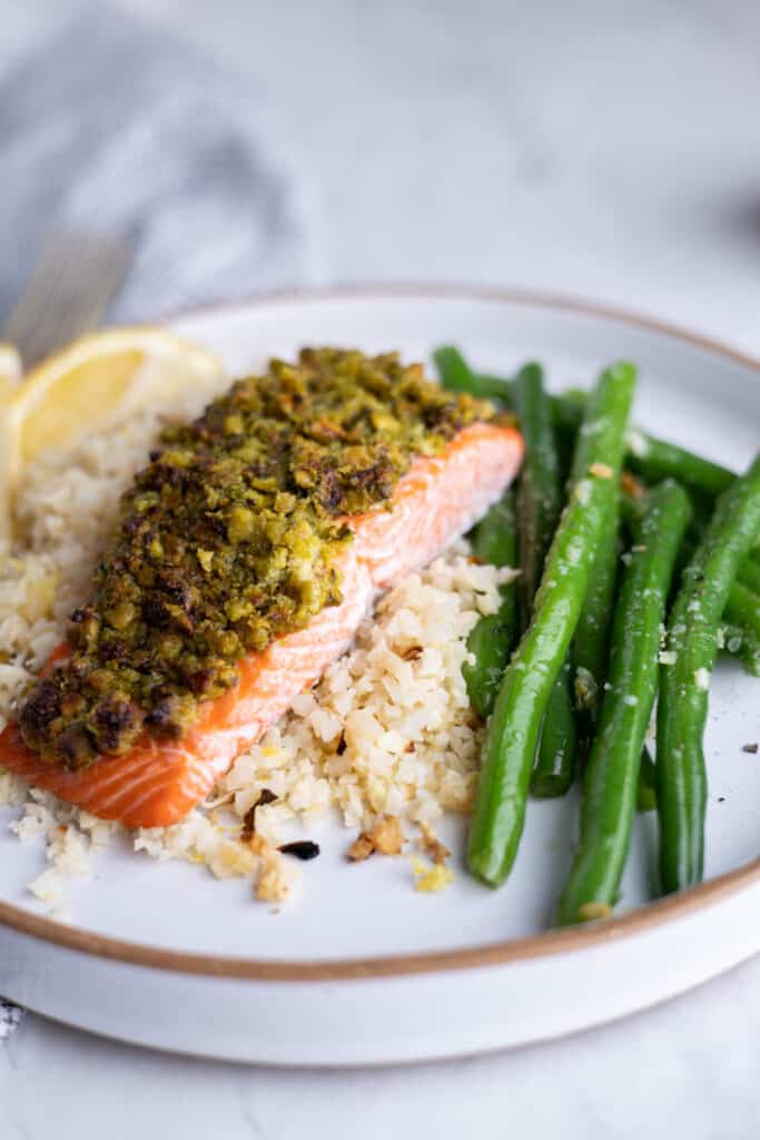 plate of cauliflower rice topped with pistachio crusted salmon filet and a side of green beans