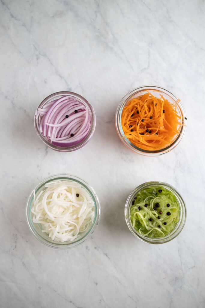 small glass jars of pickled red onions, carrot, cucumber, and taiko radish