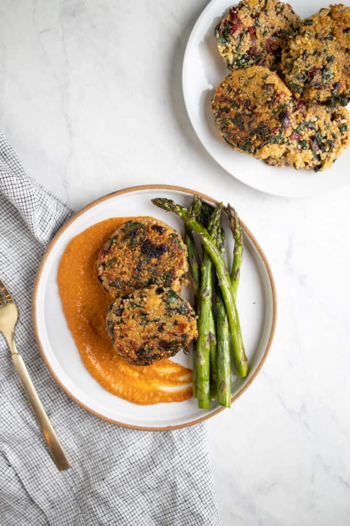 quinoa patties on a plate with romesco sauce and roasted asparagus