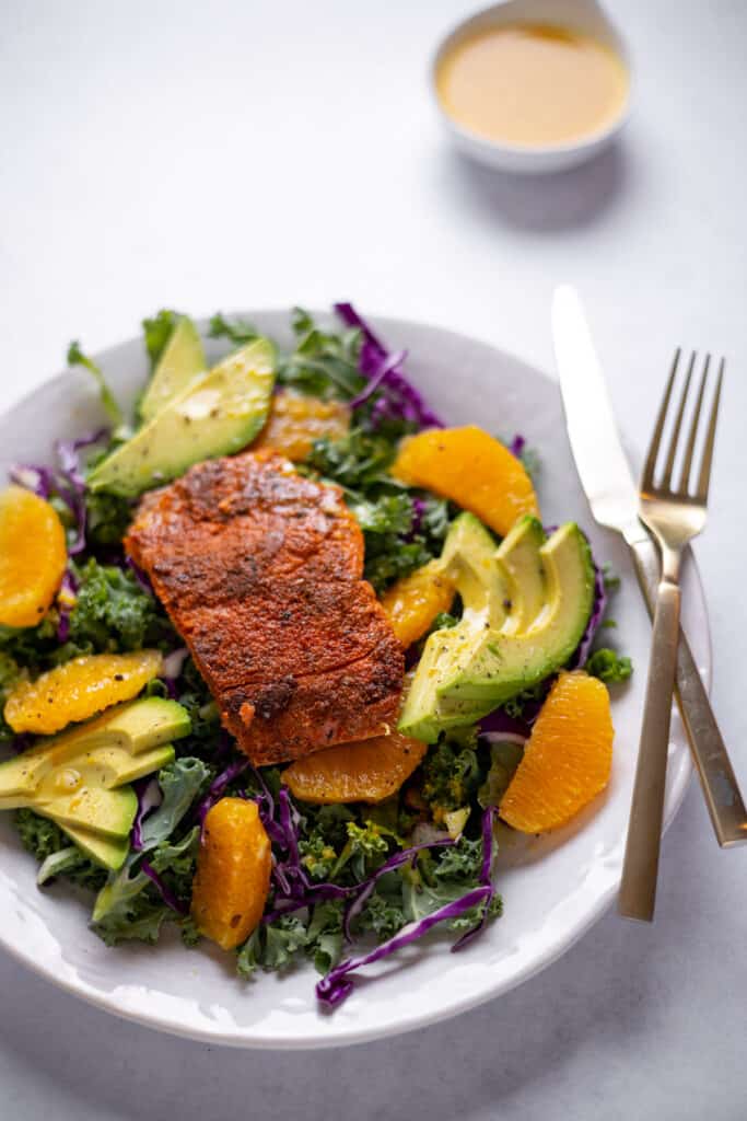 kale salad in a bowl with blackened salmon and avocado slices