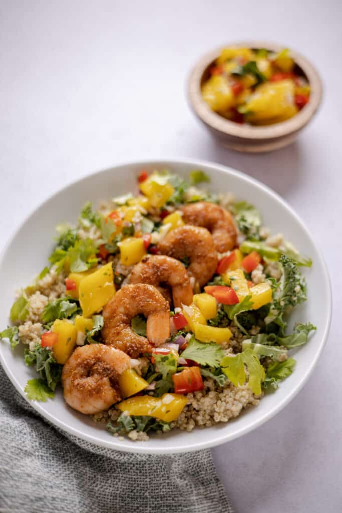 bowl filled with shrimp and mango salsa over quinoa and kale