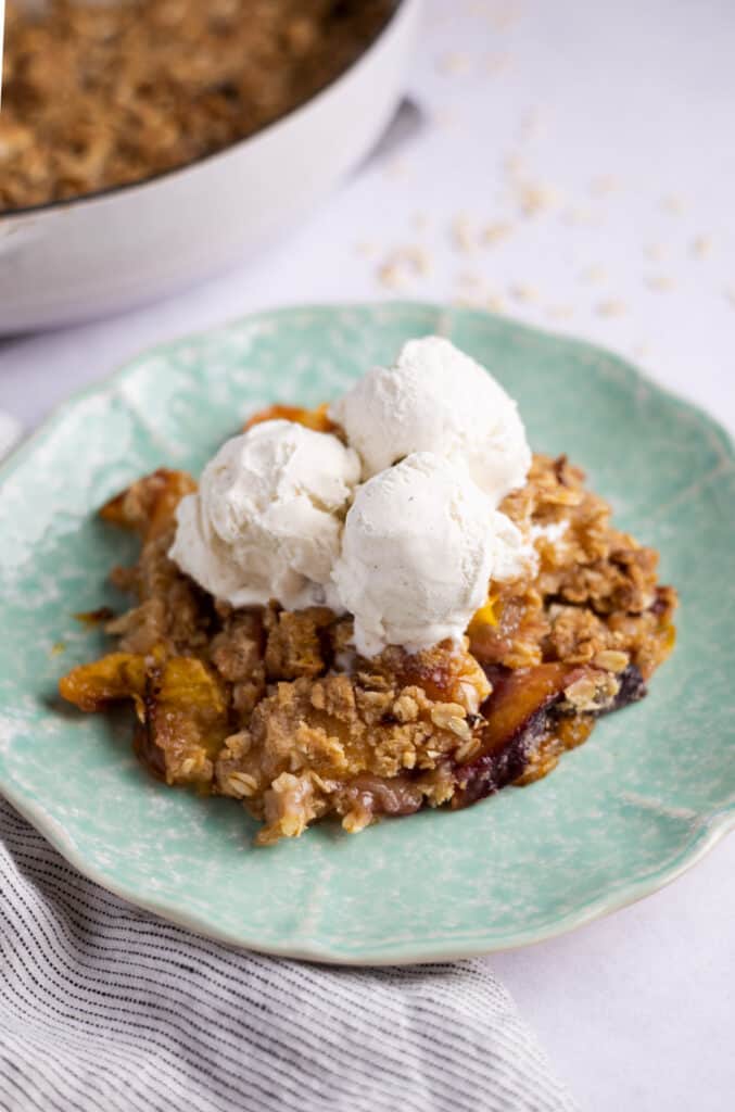 nectarine crumble on a plate with scoops of vanilla ice cream on top