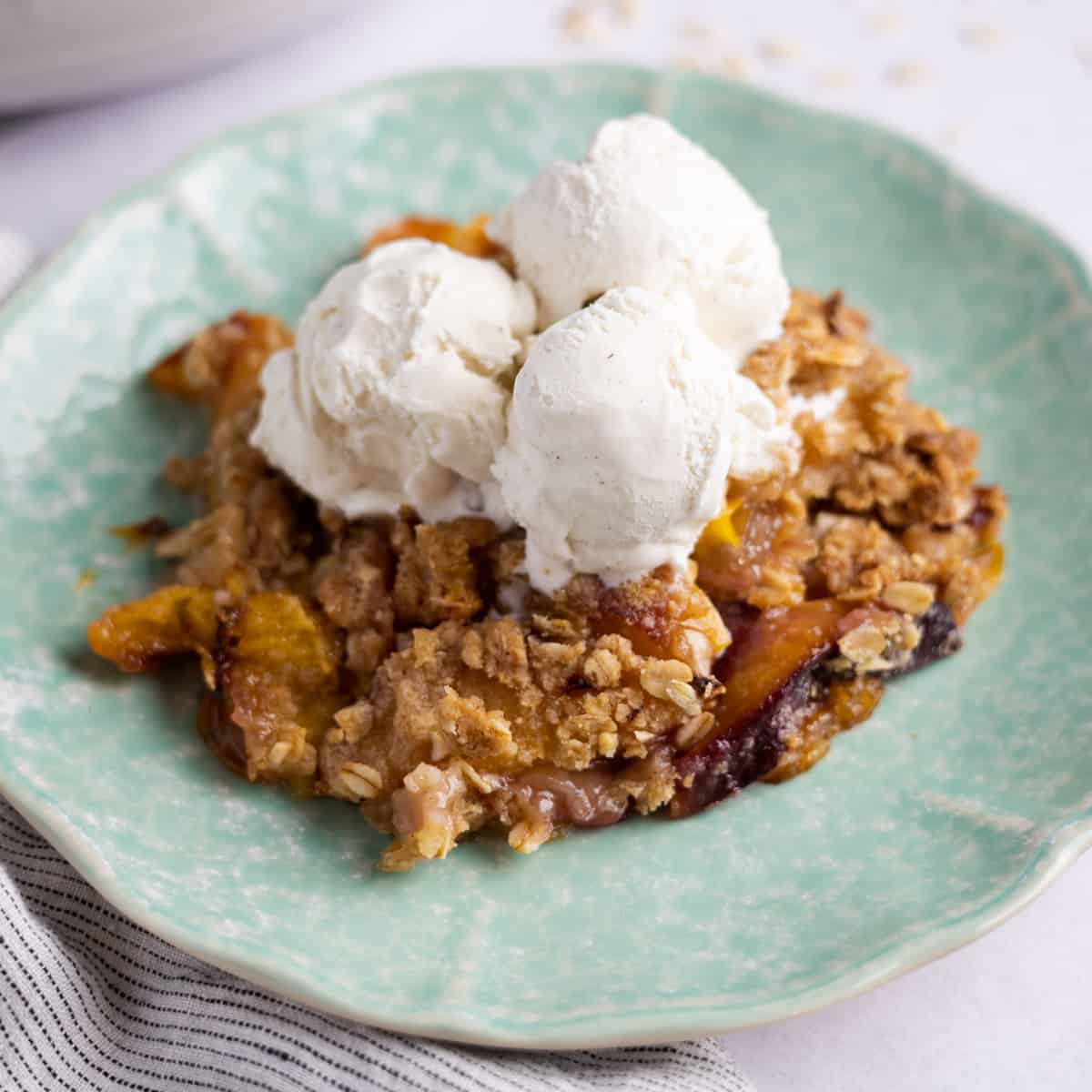 nectarine crumble on a plate with scoops of vanilla ice cream on top
