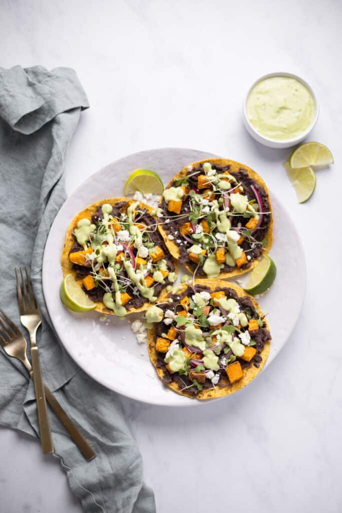 Three tostadas with black beans, sweet potatoes and drizzled with avocado crema