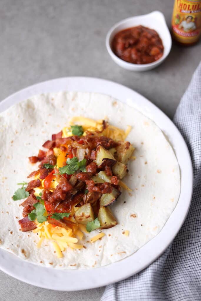 tortilla laid out with eggs, bacon, potatoes and veggies and topped with salsa