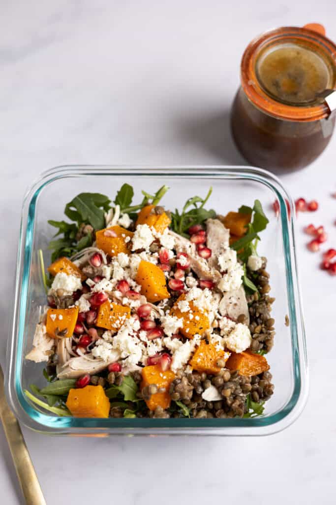 glass container with fall meal prep salad of lentils, arugula, squash, chicken and pomegranate seeds