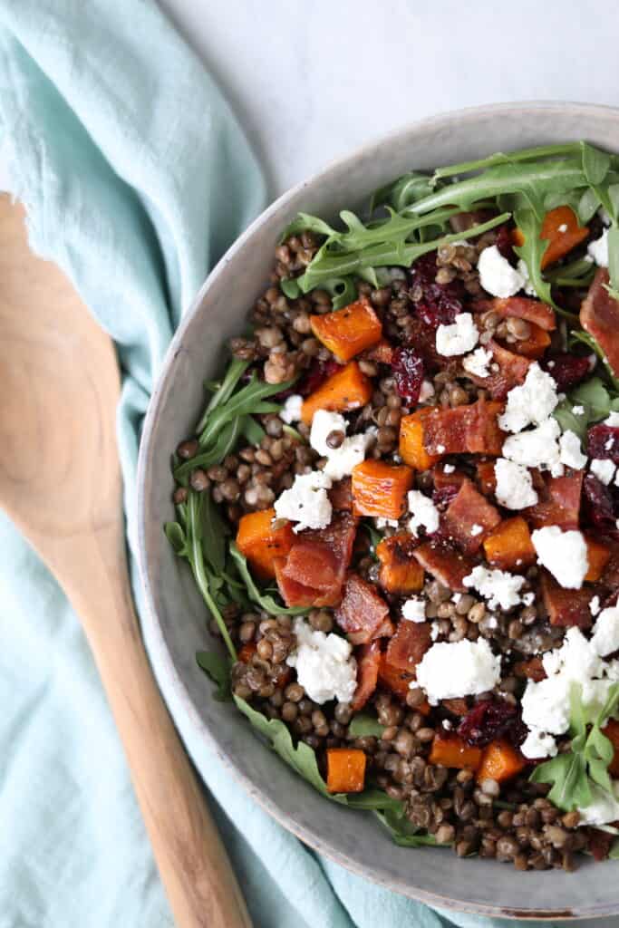 bowl filled with lentils, arugula, squash, bacon and cranberries