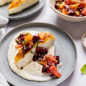 halibut filet on a bed of pureed cauliflower and topped with citrus salsa served on a blue plate.