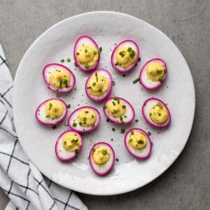 Beet deviled eggs arranged on a white serving platter.