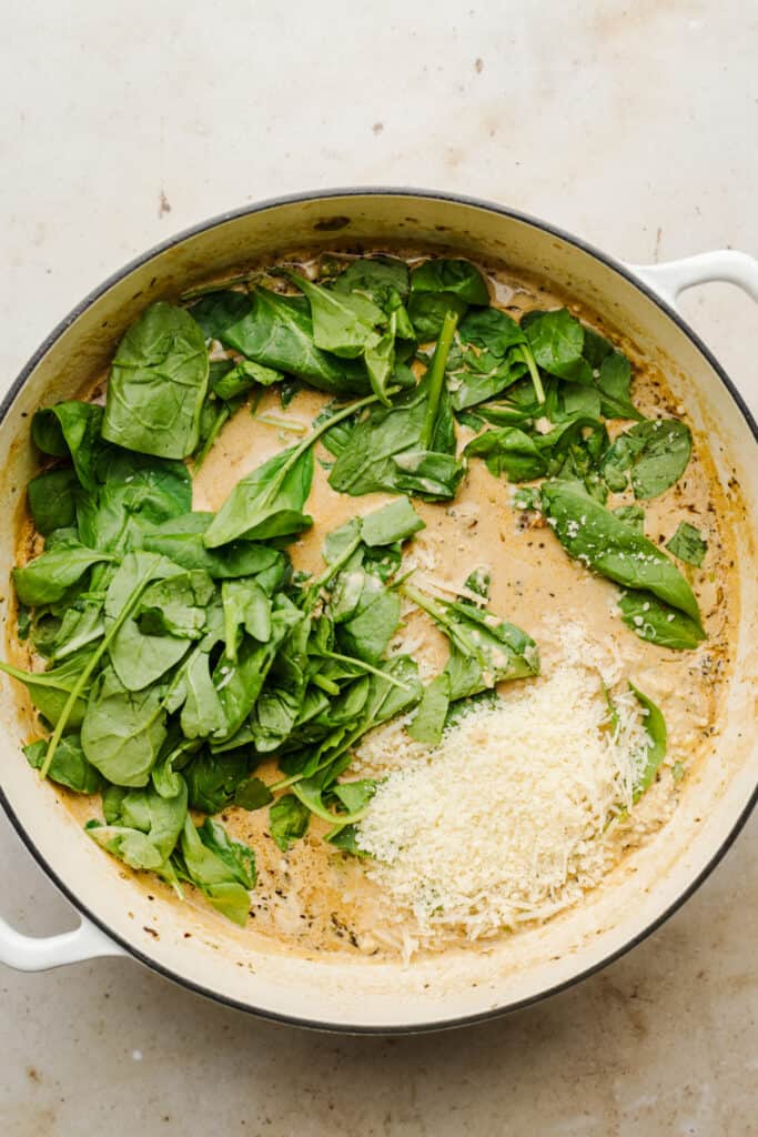 Spinach and parmesan added to sundried tomato sauce in a skillet.