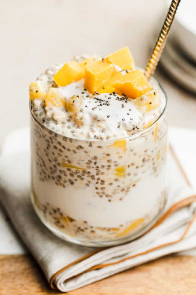 Glass filled with tropical overnight oats and topped with frozen fruit.