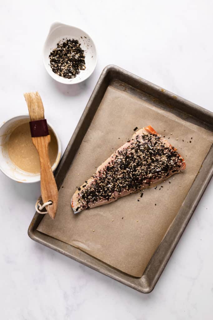 Prepped and raw furikake salmon filet on a sheet pan with parchment paper.